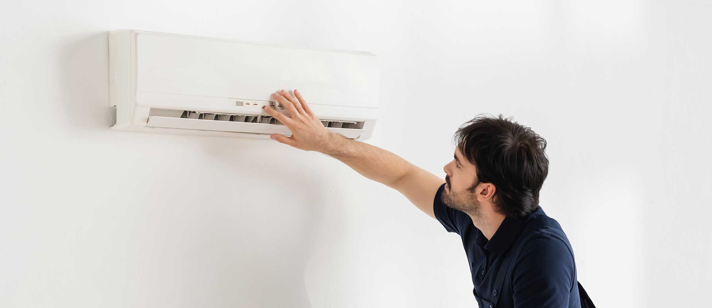 handyman in overalls standing on ladder while fixing broken air conditioner